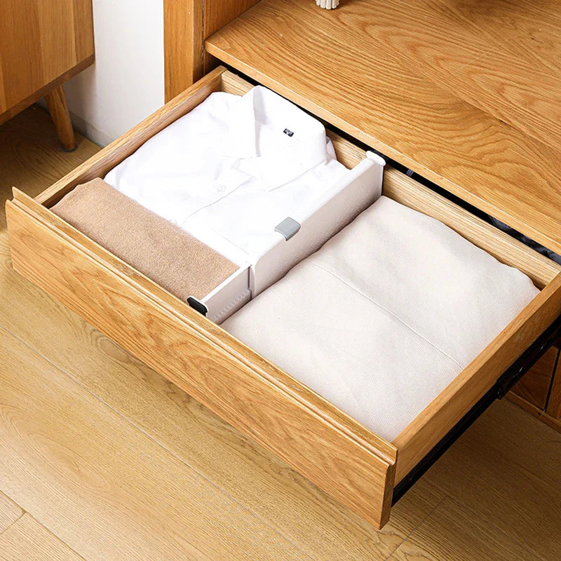 Wooden dresser drawer with a closet drawer organizer dividing folded white shirts, a tan towel, and light linens