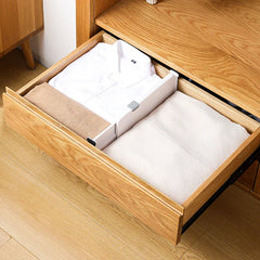 Wooden dresser drawer with a closet drawer organizer dividing folded white shirts, a tan towel, and light linens