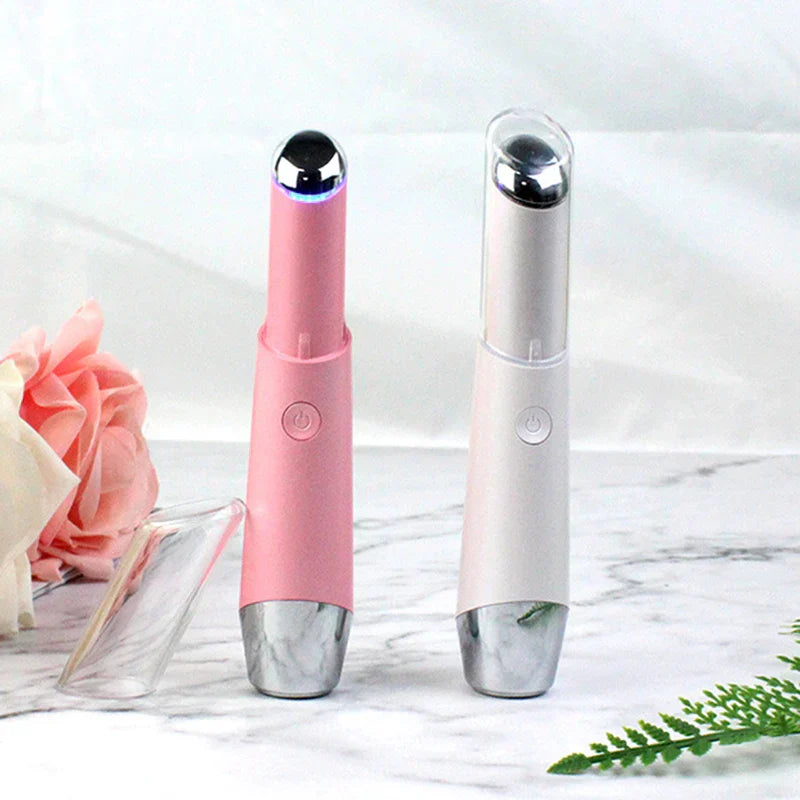 Beauty Massager Pen Tool - Two eye massager pens, one pink one white, sit on marble with a pink flower and fern nearby