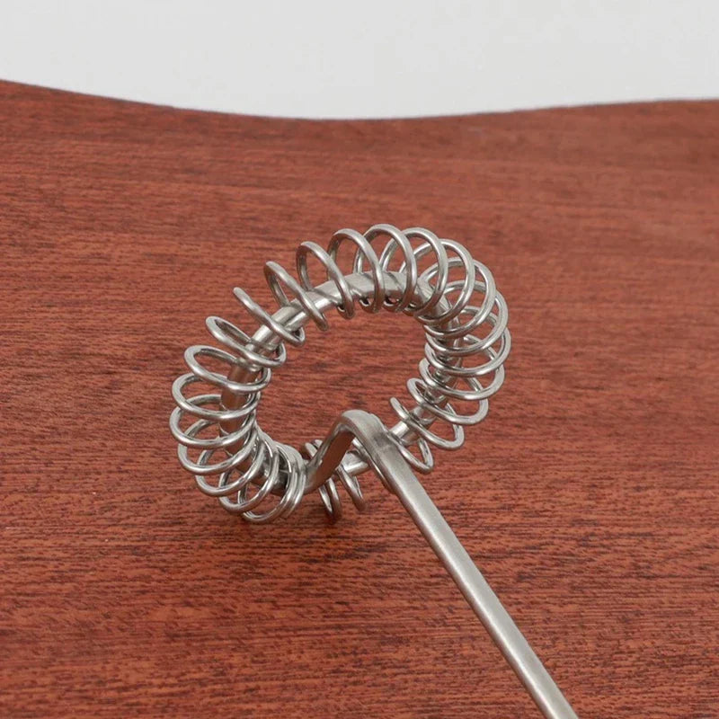 Facial Cleanser Foam Maker - Close-up of a coiled stainless steel whisk head resting on a wooden surface