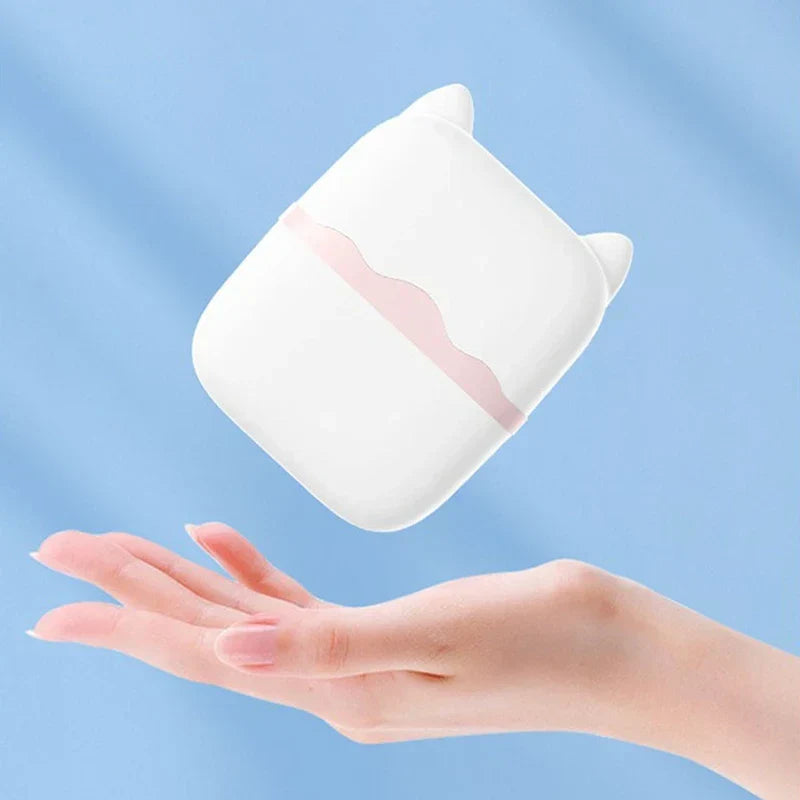Facial Ice Roller - Hand with light pink manicure holding a palm-sized white cat-shaped cosmetic tool with a pale pink wavy band, against a light blue background