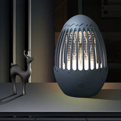 Bug Repellent Machine - Dark gray egg-shaped zapper/lamp emits warm white light, sitting on a surface beside a small stylized black deer figurine.