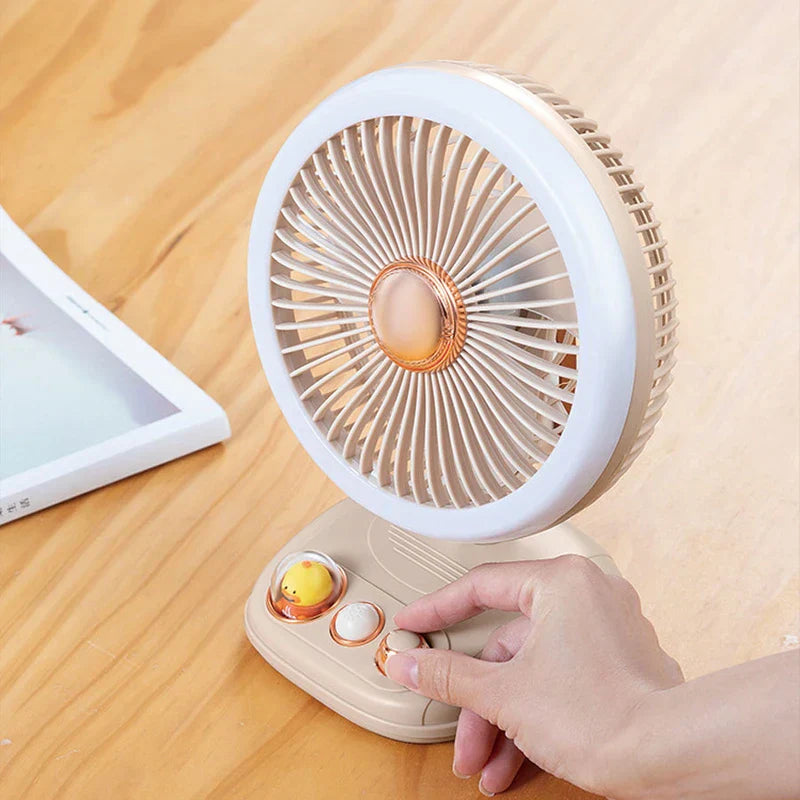 A hand adjusts a knob on a beige portable standing fan placed on a wooden table.