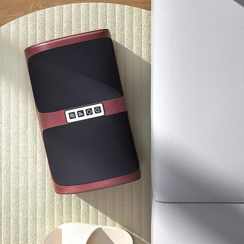 máquina masajeadora de pies - Masajeador de piernas rojo y negro sobre una superficie clara texturizada junto a muebles de color claro, con botones de control superiores visibles