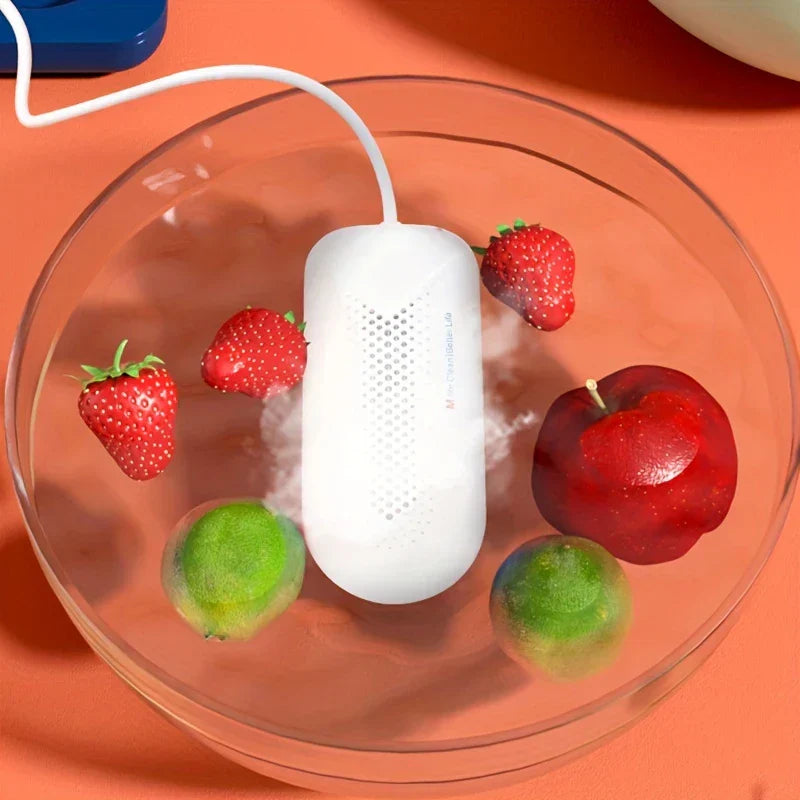 Fruit Vegetable Washing Machine - White corded electronic device submerged in a clear glass bowl of water with strawberries, limes and a red apple, mist rising from the device