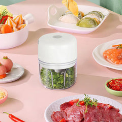 White electric garlic press sits on a pink table surrounded by prepared foods like dumplings, shrimp, and raw meat.