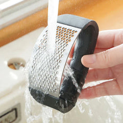 Garlic Mincer Tool - Tool being rinsed clean under running tap water over a kitchen sink