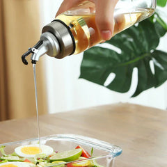 Glass Cruet - Hand tilts a glass oil bottle to pour pale yellow oil into a glass salad container.