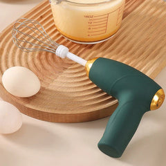 Electric Milk Frother Whisk - Green handheld electric whisk resting on a wooden board with two eggs and a glass measuring cup nearby