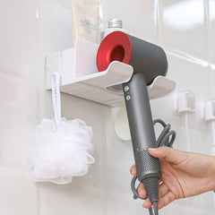 Hair Dryer Organizer - Hand holding a grey and red hairdocker, placing it into a white wall-mounted organizer attached to a tiled bathroom wall, with a loofah hanging from the organizer