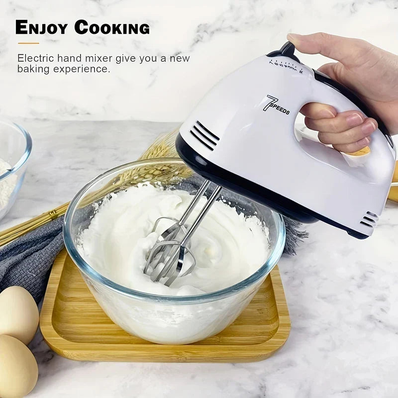 Whisk - Hand holding a white and black handheld electric mixer, mixing a white fluffy substance inside a glass bowl.