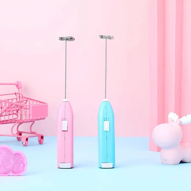 Handheld Electric Milk Frother - Two pastel-colored drink whisks displayed upright on a light blue surface with playful decorative props