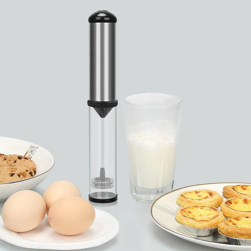 Espumador de leche eléctrico de mano: espumador colocado junto a un vaso de leche espumada, huevos frescos, galletas y tartas de huevo sobre una encimera de cocina