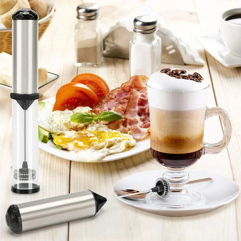 Espumador de leche eléctrico de mano: espumadores de pie y acostados junto a una bebida de café en capas, un plato de desayuno y saleros de especias sobre una superficie de madera clara