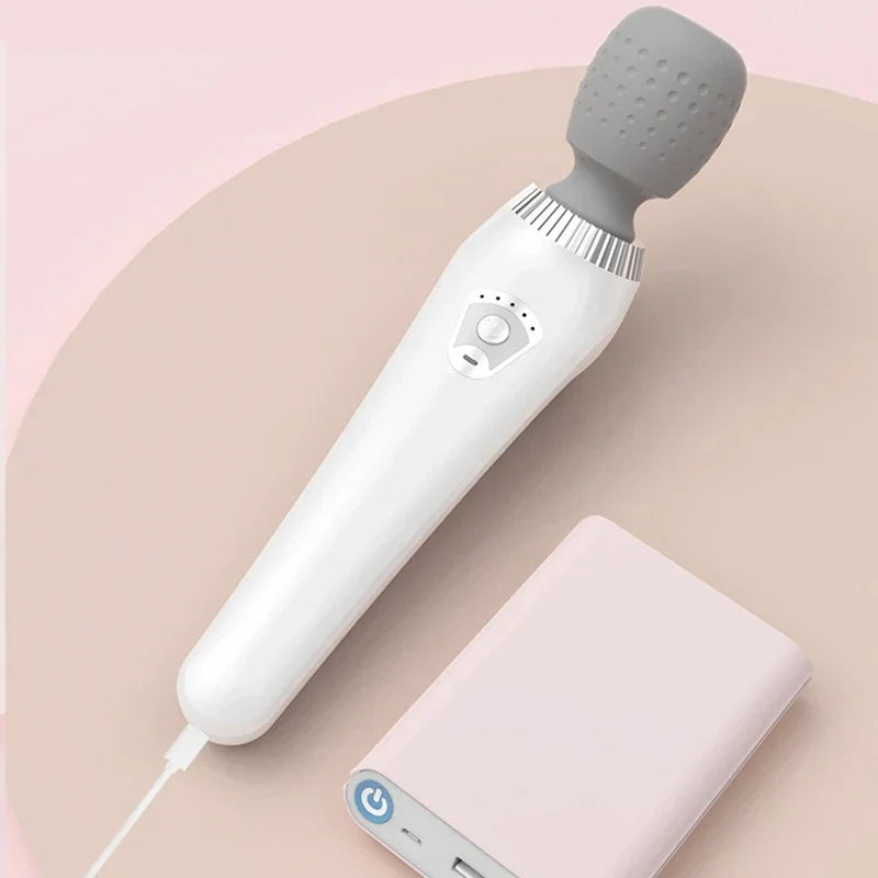 handmassagegerät für den körper - Weißes vibrierendes Handmassagegerät, eingesteckt in eine hellrosa Powerbank auf einer runden zweifarbigen rosa Oberfläche