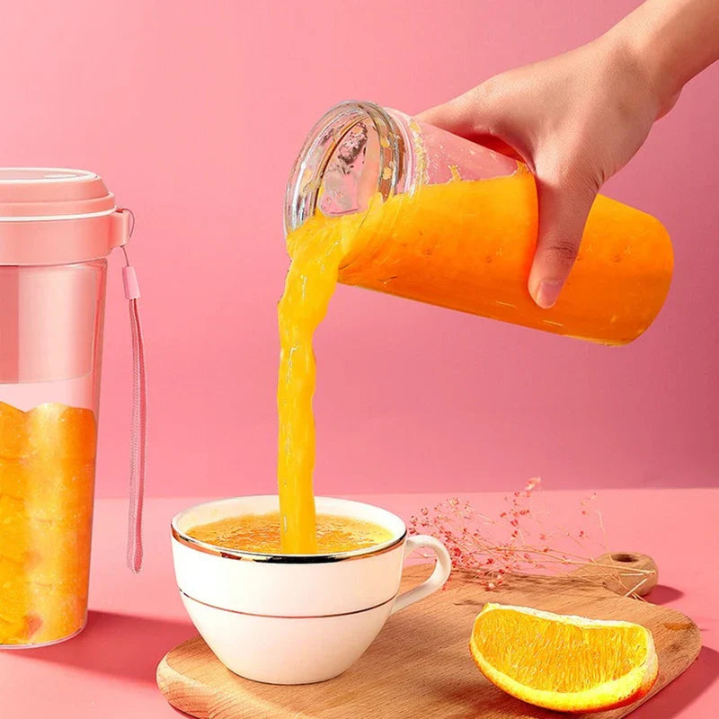 كوب خلاط محمول - يد تسكب عصير برتقال طازج مخلوط من كوب خلط في كوب أبيض، مع وجود كوب خلط آخر ممتلئ إلى اليسار