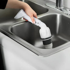 Power Scrubber - A hand holds the white cleaning tool over a stainless steel kitchen sink, with the tool head facing down and rinsing water through its outlet.