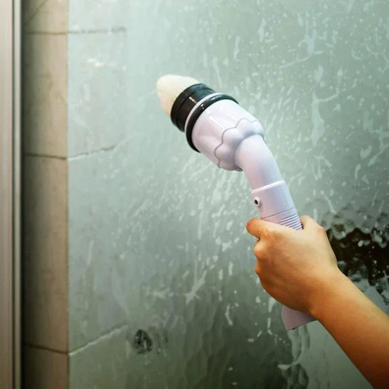 Power Scrubber - A hand holds the white cleaning tool with a light-colored brush head attached, positioned against a soapy glass shower surface.