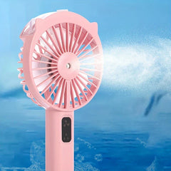 Handheld Misting Fan - Close-up of pink handheld fan emitting a fine water mist spray against a blue background.