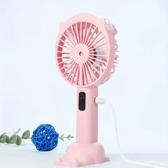 Handheld Misting Fan - Pink handheld spray fan on cat-themed stand, charging cable plugged in, blue wicker ball and greenery nearby