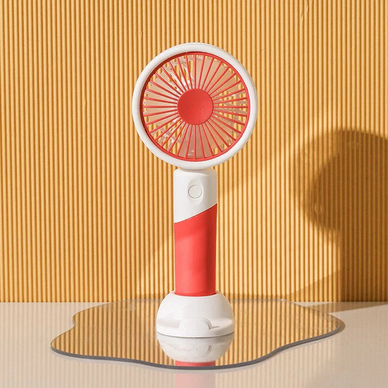 Red handheld mini fan with white stand rests on a wavy mirrored surface against ribbed yellow wall