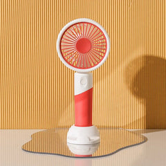 Red handheld mini fan with white stand rests on a wavy mirrored surface against ribbed yellow wall