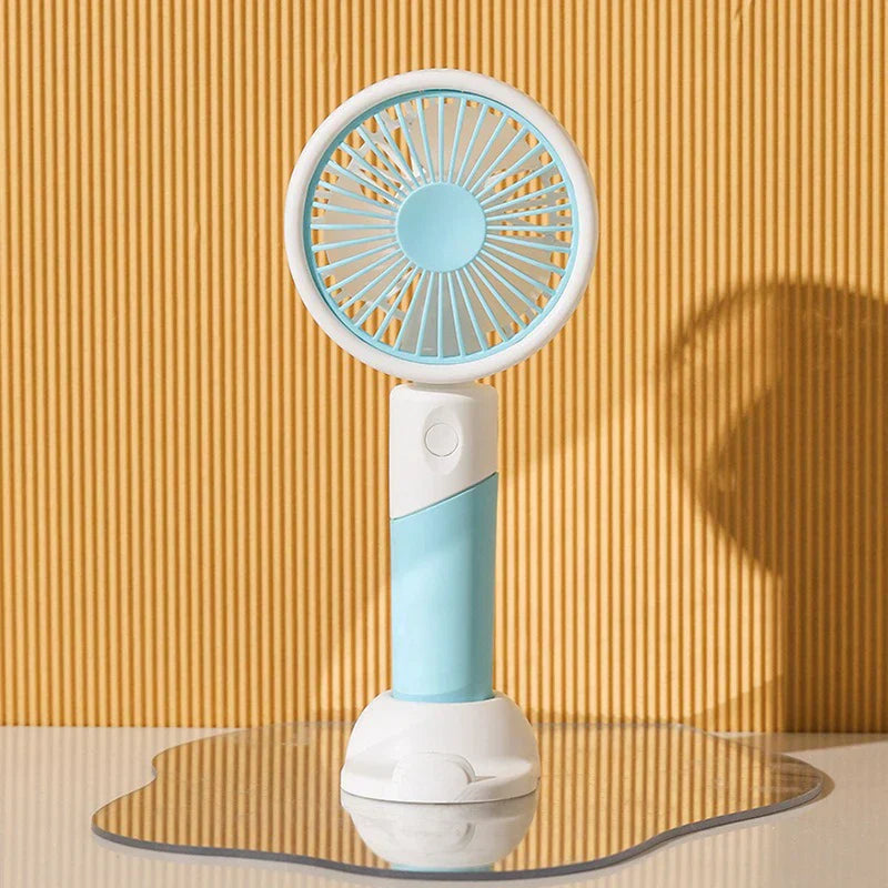 Light blue handheld mini fan with white stand rests on a wavy mirrored surface against ribbed yellow wall