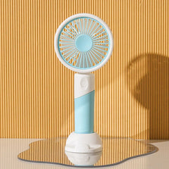 Light blue handheld mini fan with white stand rests on a wavy mirrored surface against ribbed yellow wall