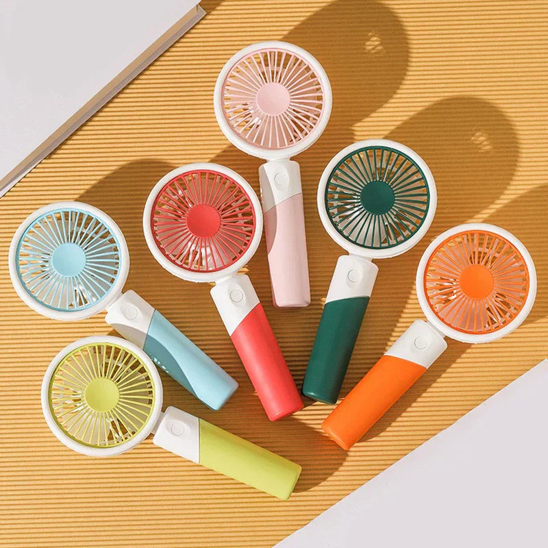 Mini Fan - Six handheld fans in different colors, flat lay on a vertical ribbed yellow surface