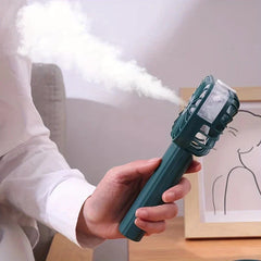 Mist Sprayer - Close-up of a hand holding a dark green handheld misting fan that emits a stream of white mist.