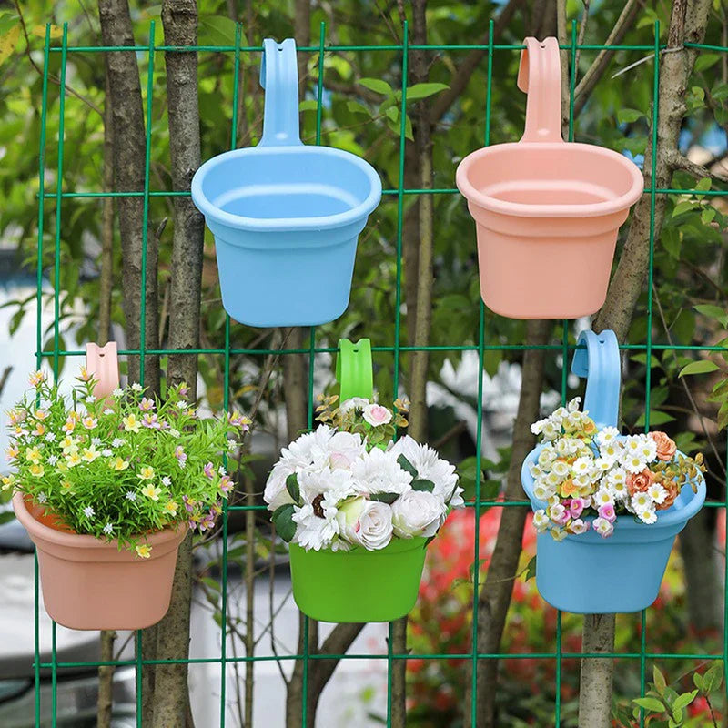 Basket Planter - Multiple colored hanging planters, some holding faux flowers, hung on a green wire mesh fence with trees behind