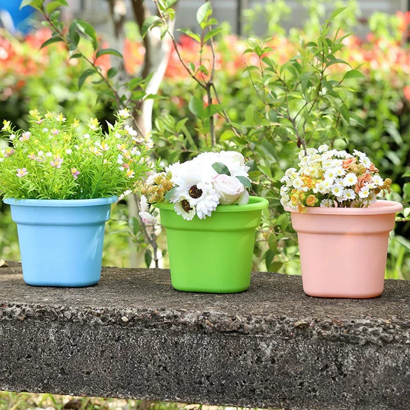Basket Planter - Three small plastic planters holding faux flowers, sitting on a rough gray concrete ledge with green foliage behind