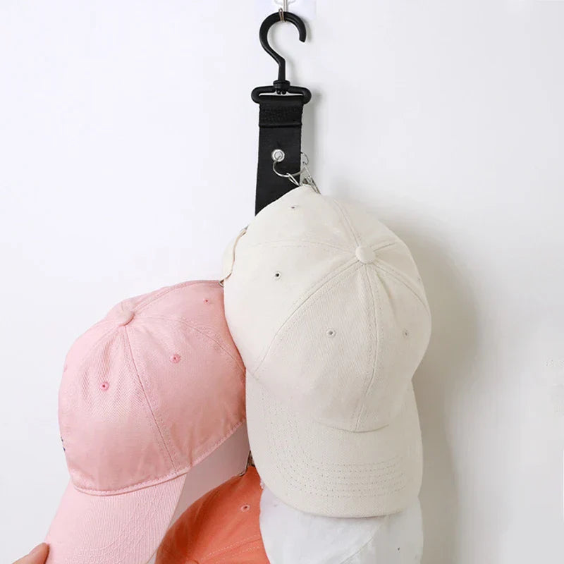 Organizador de gorras: correa colgante negra con clips metálicos sosteniendo varias gorras de béisbol contra una pared blanca