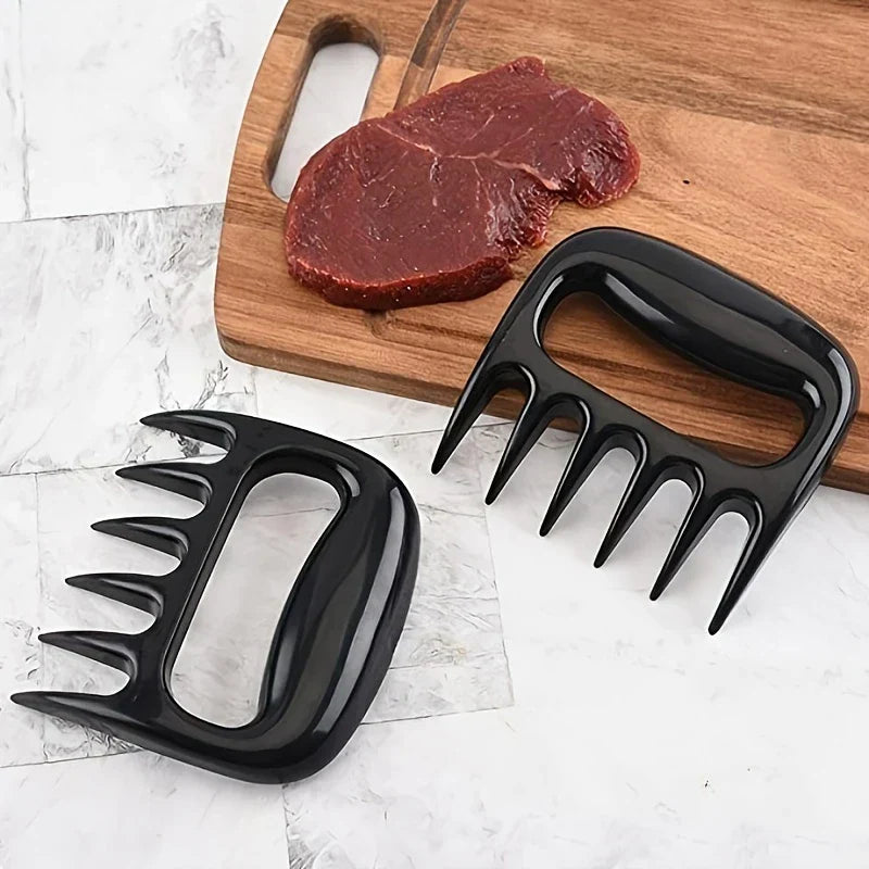 Pulled Pork Shredder Claws - Pair of black meat shredding tools resting next to a raw beef steak on a wooden cutting board over a marble countertop