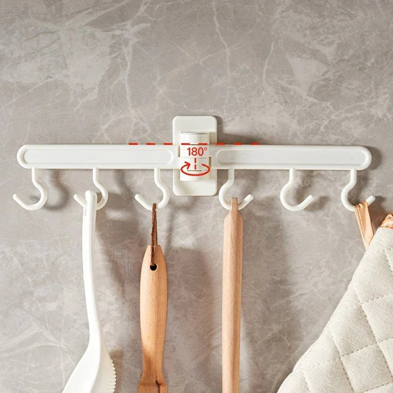 Adhesive Wall Hooks - Wall-mounted white plastic hook rack with 6 hooks, 180° rotation indicator, holding kitchen utensils and a padded fabric item