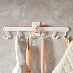 Adhesive Wall Hooks - Wall-mounted white plastic hook rack with 6 hooks, 180° rotation indicator, holding kitchen utensils and a padded fabric item