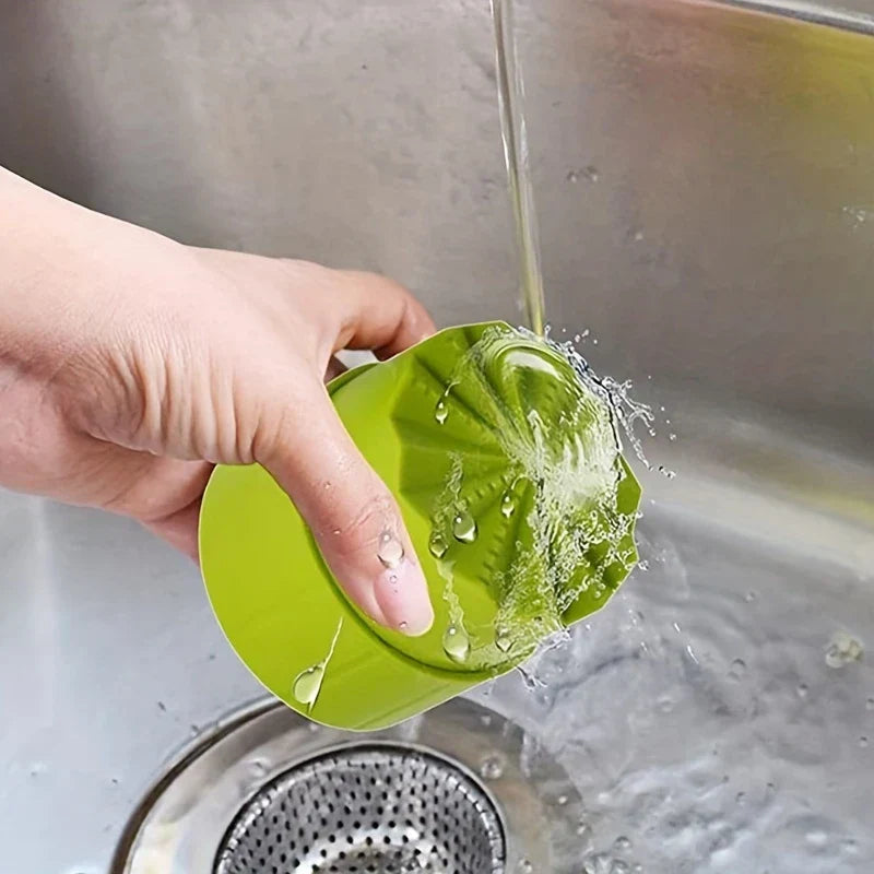 Garlic Press Mincer - A hand holds a green citrus juicer under running water over a stainless steel sink.