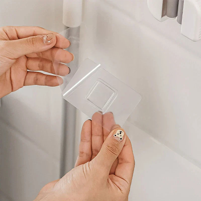 Mop Broom Holder - Two hands holding a clear adhesive mounting tab for the mop holder