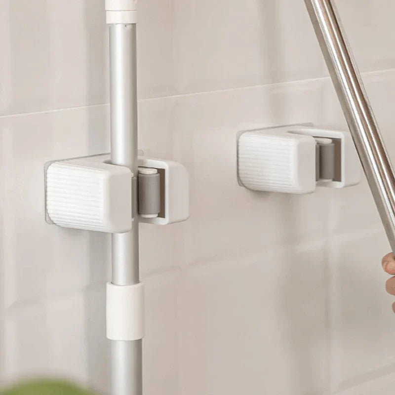 Mop Broom Holder - Two installed white mop holders on a tiled wall; one holding a gray pole, one empty with another pole nearby