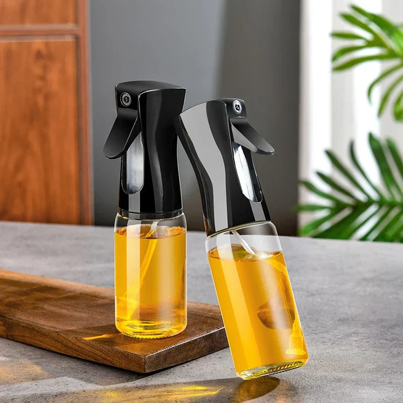 Mister Bottle - Two glass oil spray bottles with black pump tops, one upright on wood board, one tilted, both holding yellow liquid, on gray countertop.