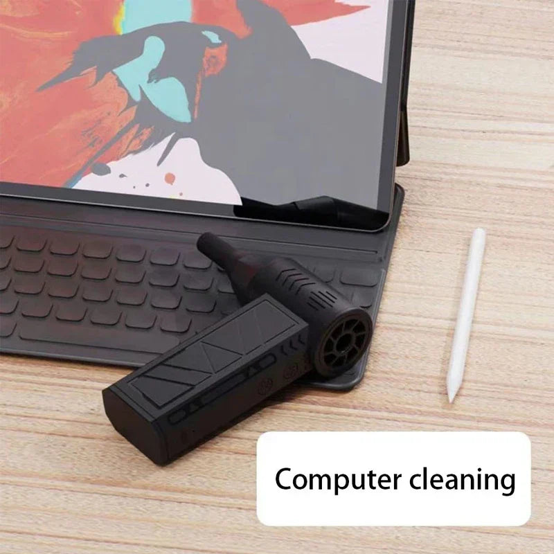 ventilador circulador de aire - Mini soplador de aire descansando sobre un teclado de tableta junto a un lápiz táctil en un escritorio de madera, con etiqueta 'Limpieza de computadoras'