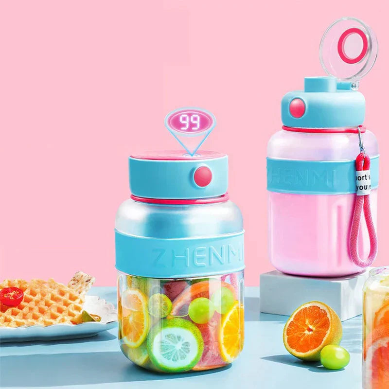 Two smoothie maker tumbler bottles, one loaded with cut fruit, sit on a pale blue table beside citrus fruit and a waffle plate against a pink background