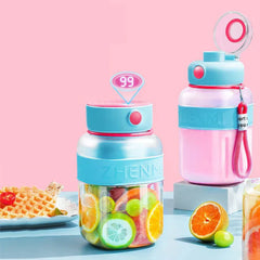 Two smoothie maker tumbler bottles, one loaded with cut fruit, sit on a pale blue table beside citrus fruit and a waffle plate against a pink background