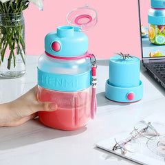 Hand holds a smoothie maker tumbler bottle with pink drink inside; a blender base with blade sits on a white marble table next to it