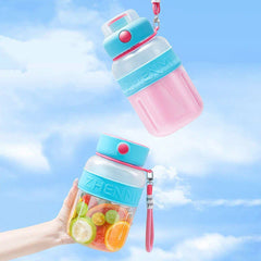 Two smoothie maker tumbler bottles hang and are held by a hand, with fruit pieces in the lower bottle, against a bright blue sky with clouds.