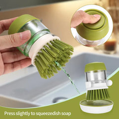 Pot Scrubber Brush - A hand presses the top of a soap-dispensing dish brush, with soap extruding from the bristles; a seated brush is shown inset bottom right.