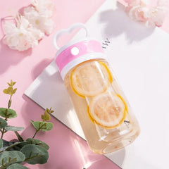 Insulated Coffee Travel Mug - Clear travel tumbler with pink lid band holding lemon-infused water, styled with eucalyptus and flowers on a pink surface
