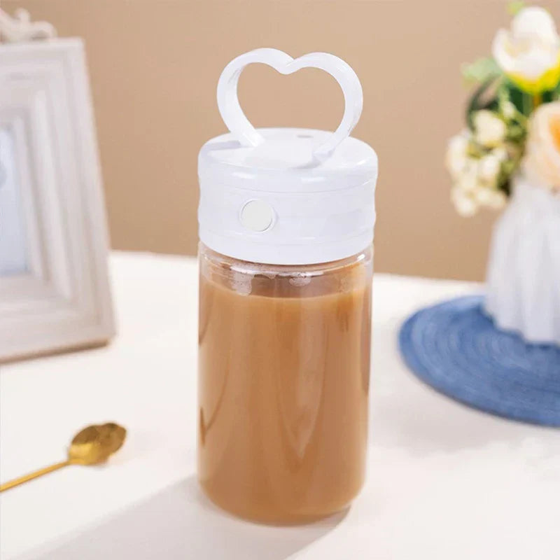Insulated Coffee Travel Mug - White-lidded travel tumbler with heart handle filled with coffee, placed on a tabletop with a gold spoon and decorative accents