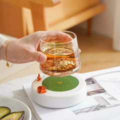 Insulated Mug - A hand lifts a glass of amber liquid above the white coaster with green heating surface.