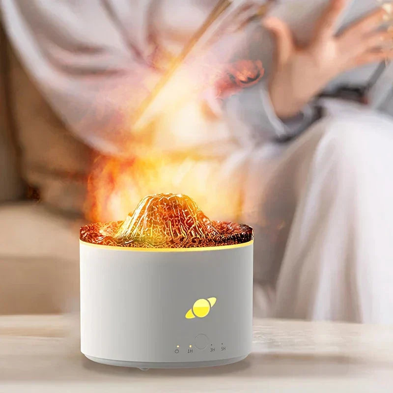 difusor humidificador de llama - Humidificador cilíndrico blanco con parte superior en forma de volcán iluminada que emite niebla, colocado sobre una mesa clara con una persona al fondo desenfocada